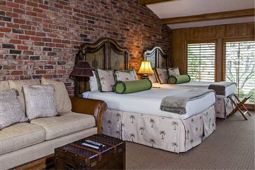 Double queen beds and couch with large windows and brick wall in hotel room